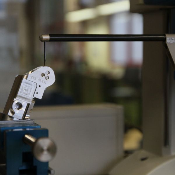 Ein Präzisionstaster prüft ein in einem Schraubstock eingespanntes Metallteil, wahrscheinlich zur Qualitätskontrolle oder für Messungen in der Industrie oder im Labor.