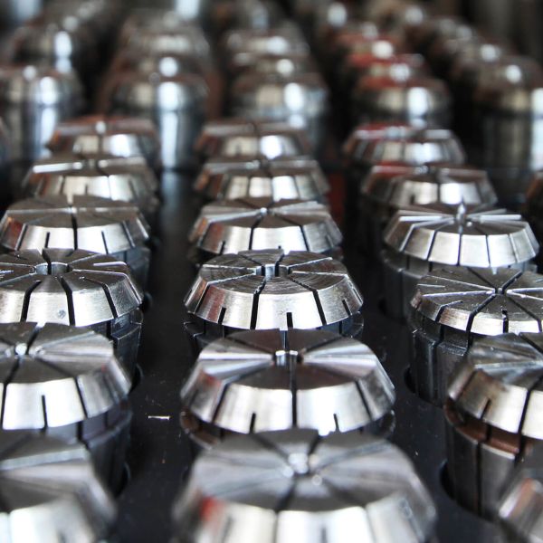 Ein Schwarz-Weiß-Foto zeigt mehrere Frauen, die an Werkbänken sitzen, Maschinen bedienen und unter Schreibtischlampen in einer Fabrik kleine Teile zusammenbauen.