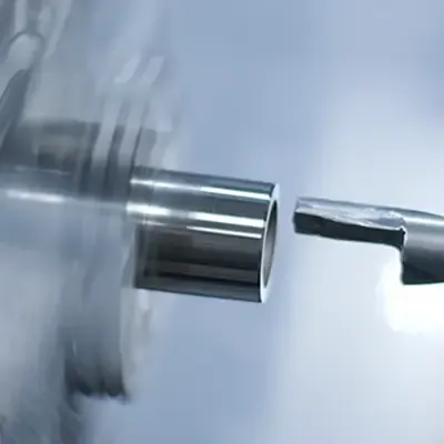 Nahaufnahme eines Metallzylinders, der auf einer Drehmaschine bearbeitet wird, mit einem Schneidewerkzeug in der Nähe seiner Kante und einer Bewegungsunschärfe, die die Drehung des Zylinders zeigt.
