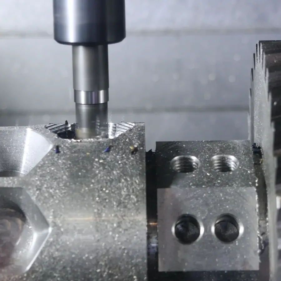 Nahaufnahme einer CNC-Fräsmaschine, die ein Metallwerkstück fräst, mit sichtbaren Zahnrädern und sechseckigen Mustern auf der Oberfläche, die während des Bearbeitungsprozesses Metallspäne erzeugen.