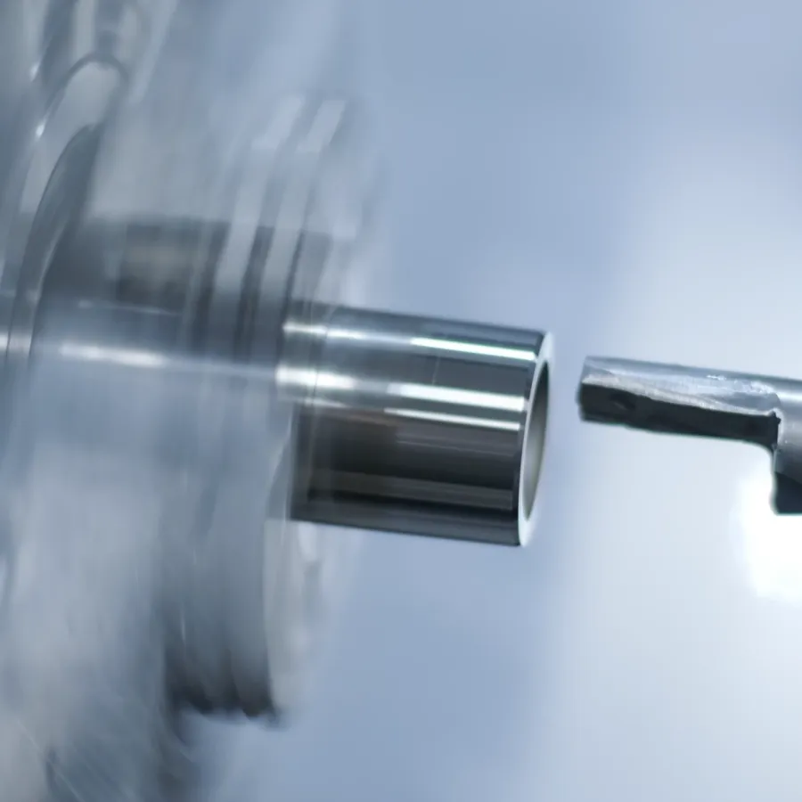 Nah&shy;auf&shy;nahme einer CNC-Dreh&shy;maschine, die einen rotierenden Metall&shy;zylinder schneidet und dabei glatte und glänzende Ober&shy;flächen&shy;konturen erzeugt. Der Hinter&shy;grund ist unscharf und unter&shy;streicht den Präzisions&shy;metall&shy;bearbeitungs&shy;prozess.