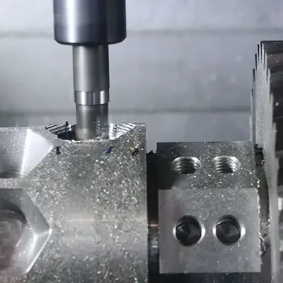 Nahaufnahme einer CNC-Fräsmaschine, die Gewinde in einen Metallblock schneidet, wobei um den Schnittbereich herum Metallspäne sichtbar sind.