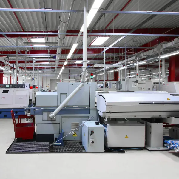 Ein modernes, hell erleuchtetes Fabrikinnere mit großen Industriemaschinen und Geräten, die in Reihen unter einer hohen Decke mit freiliegenden Balken und Lichtern angeordnet sind. Der Boden ist sauber und es sind keine Arbeiter anwesend.